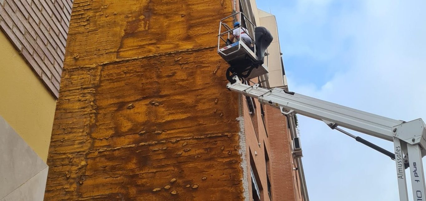 Examinando Fachada con máquina Trabajador en un andamio limpiando la fachada de un edificio.